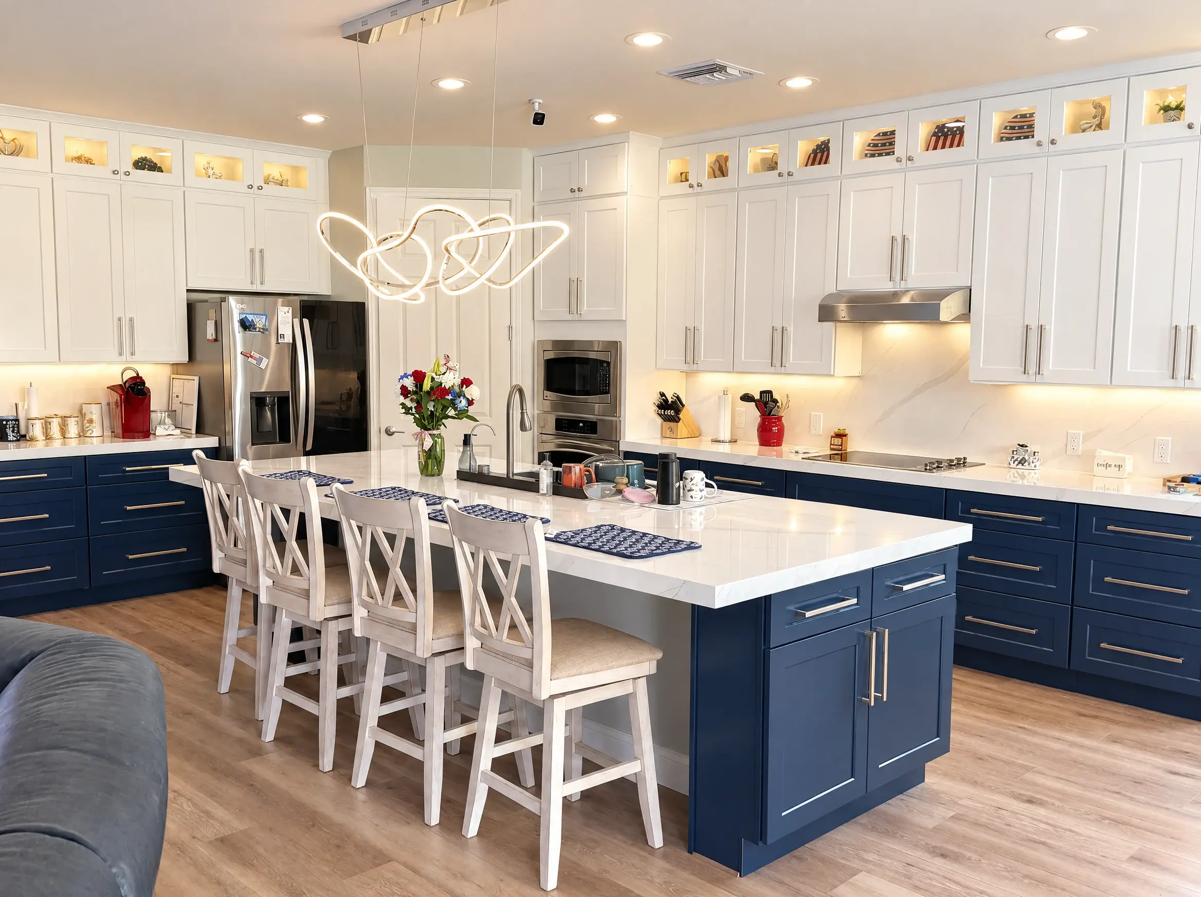 Collaborative Construction’s completed kitchen with white upper cabinets, navy lower cabinets, a quartz island and four cross-back stools. AI-relit daytime, lights-on view.